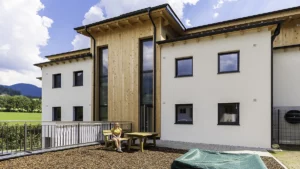 Person sitzt auf Holzbank und im Hintergrund ist die Wohnanlage Pfarrwerfen zu sehen